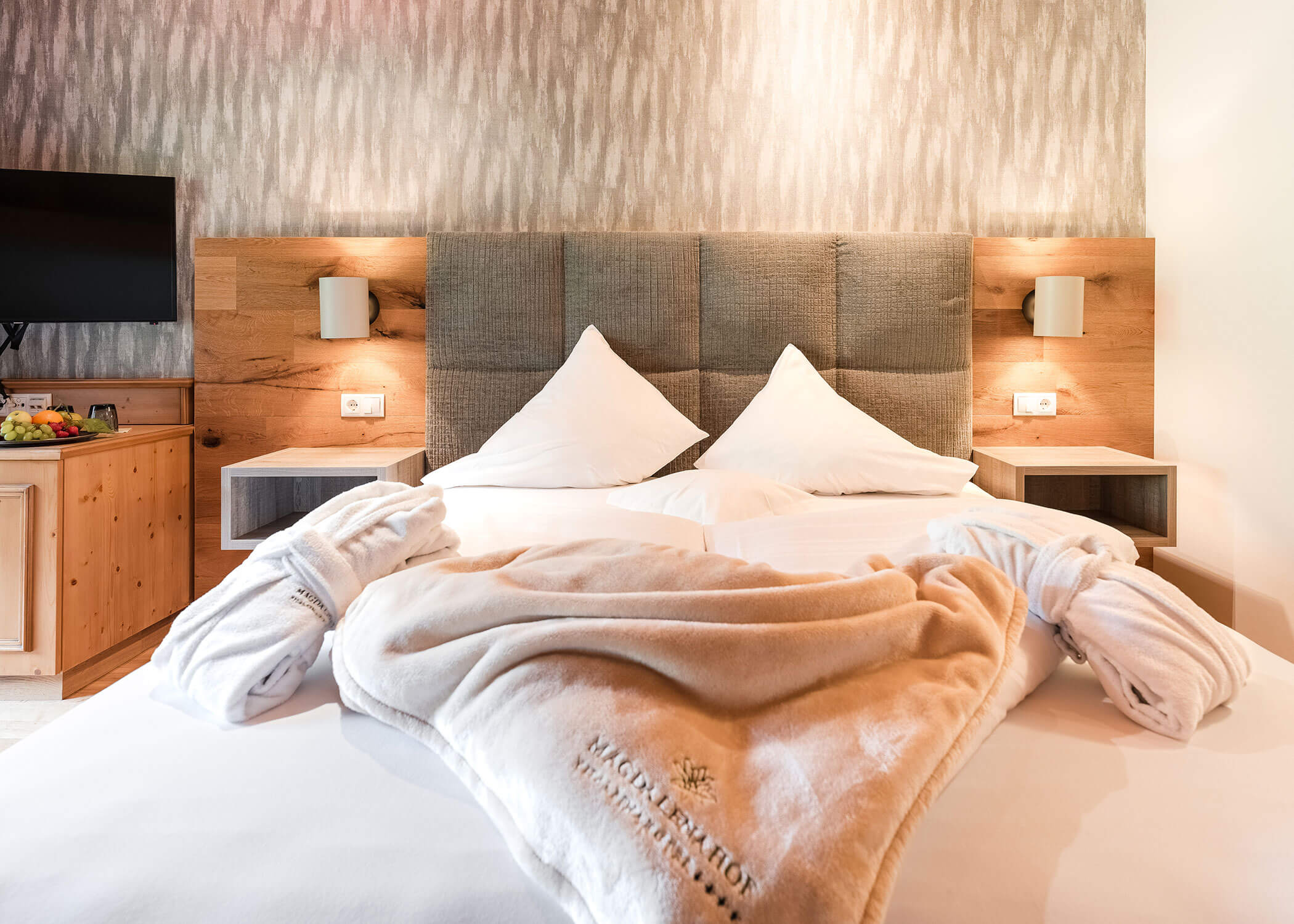 Hotelzimmer mit sauberem Doppelbett, zwei Bademänteln und modernem Holzdekor. - Hotel Magdalenahof