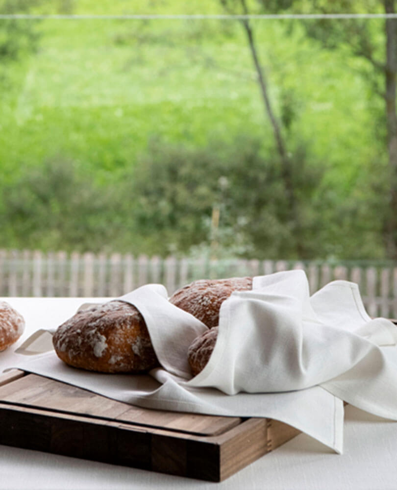 Zwei Brote, teilweise mit einem weißen Tuch bedeckt, auf einem Holzbrett, mit einem grünen Feld im Hintergrund. - Hotel Magdalenahof