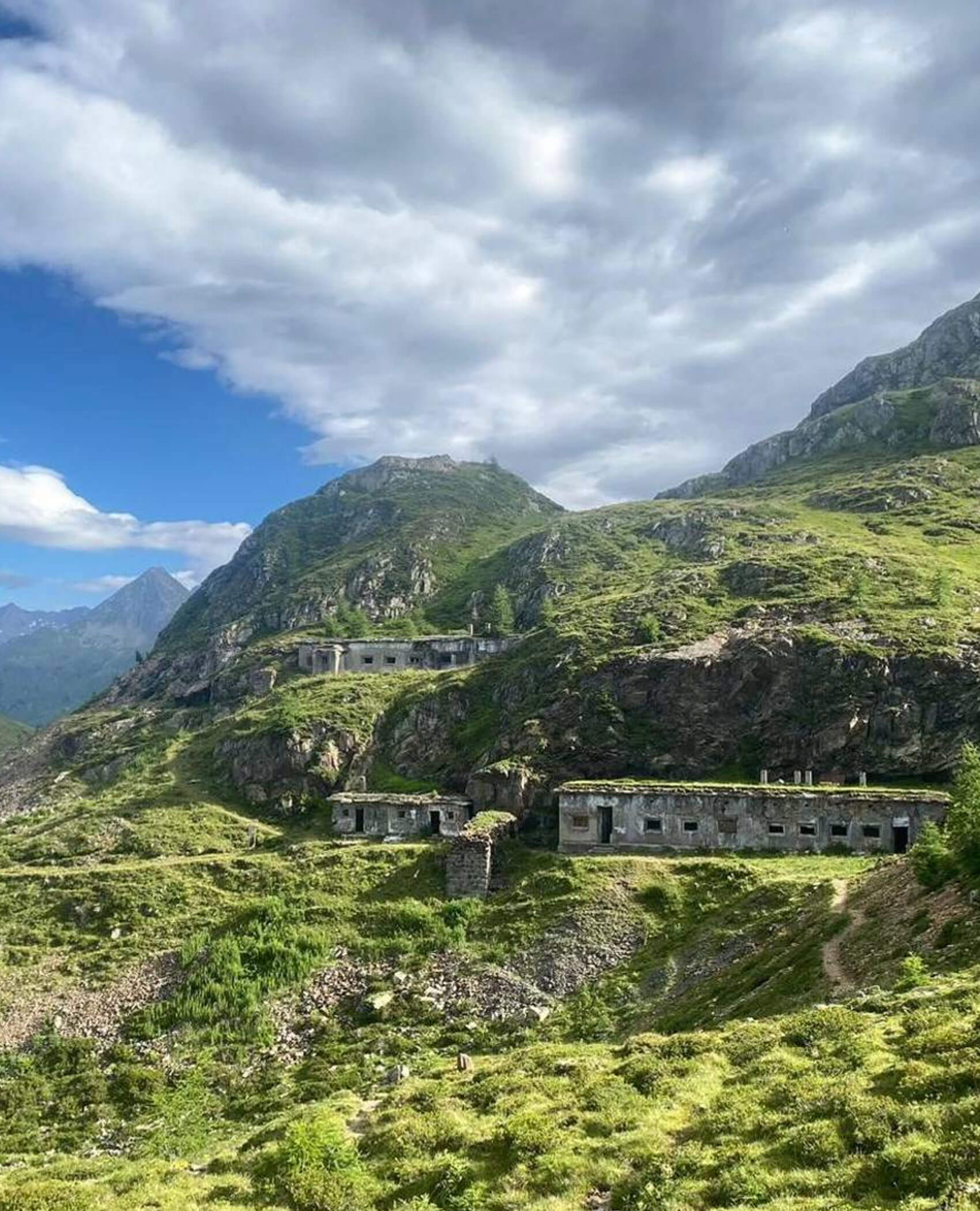 Verlassene Steingebäude an einem üppig grünen Berghang unter einem teilweise bewölkten Himmel. - Hotel Magdalenahof
