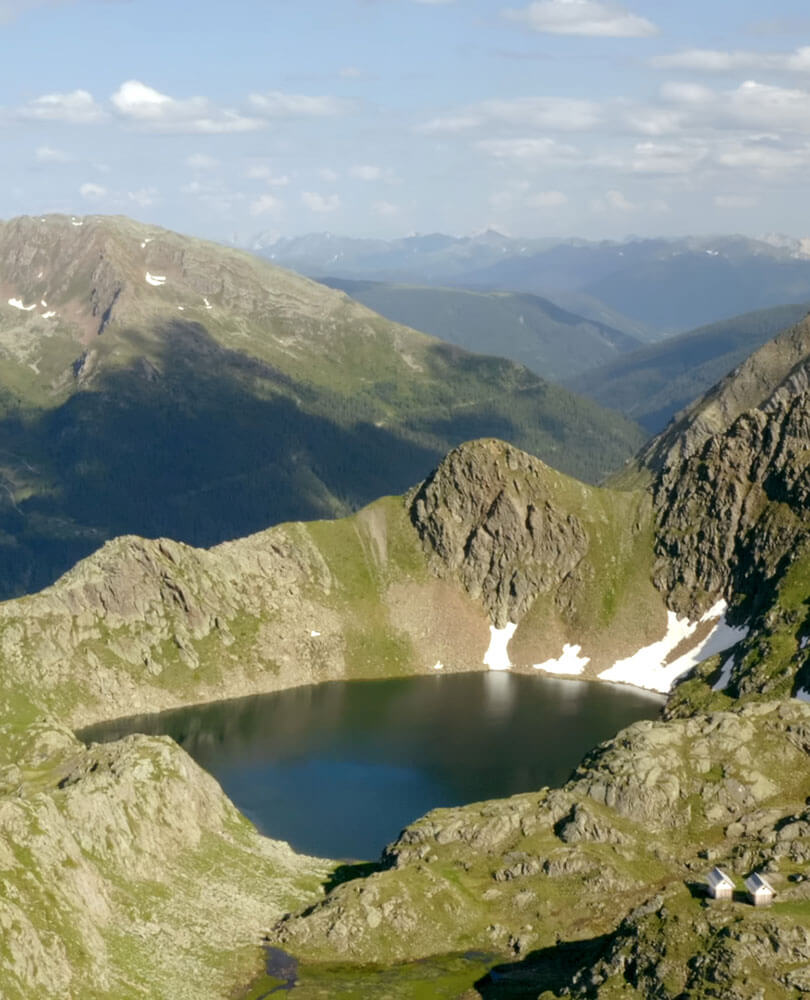 Ein Bergsee, umgeben von felsigen, grünen Hügeln unter einem teilweise bewölkten Himmel. - Hotel Magdalenahof