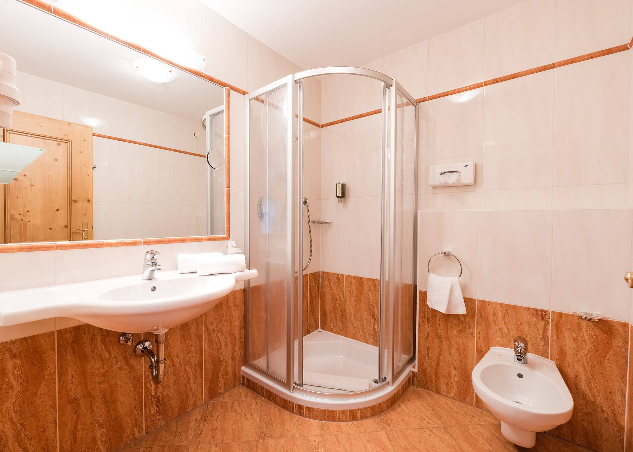 Modernes Badezimmer mit Eckdusche, Wandwaschbecken, Bidet, großem Spiegel und pfirsichfarbenem Fliesendekor. - Hotel Magdalenahof