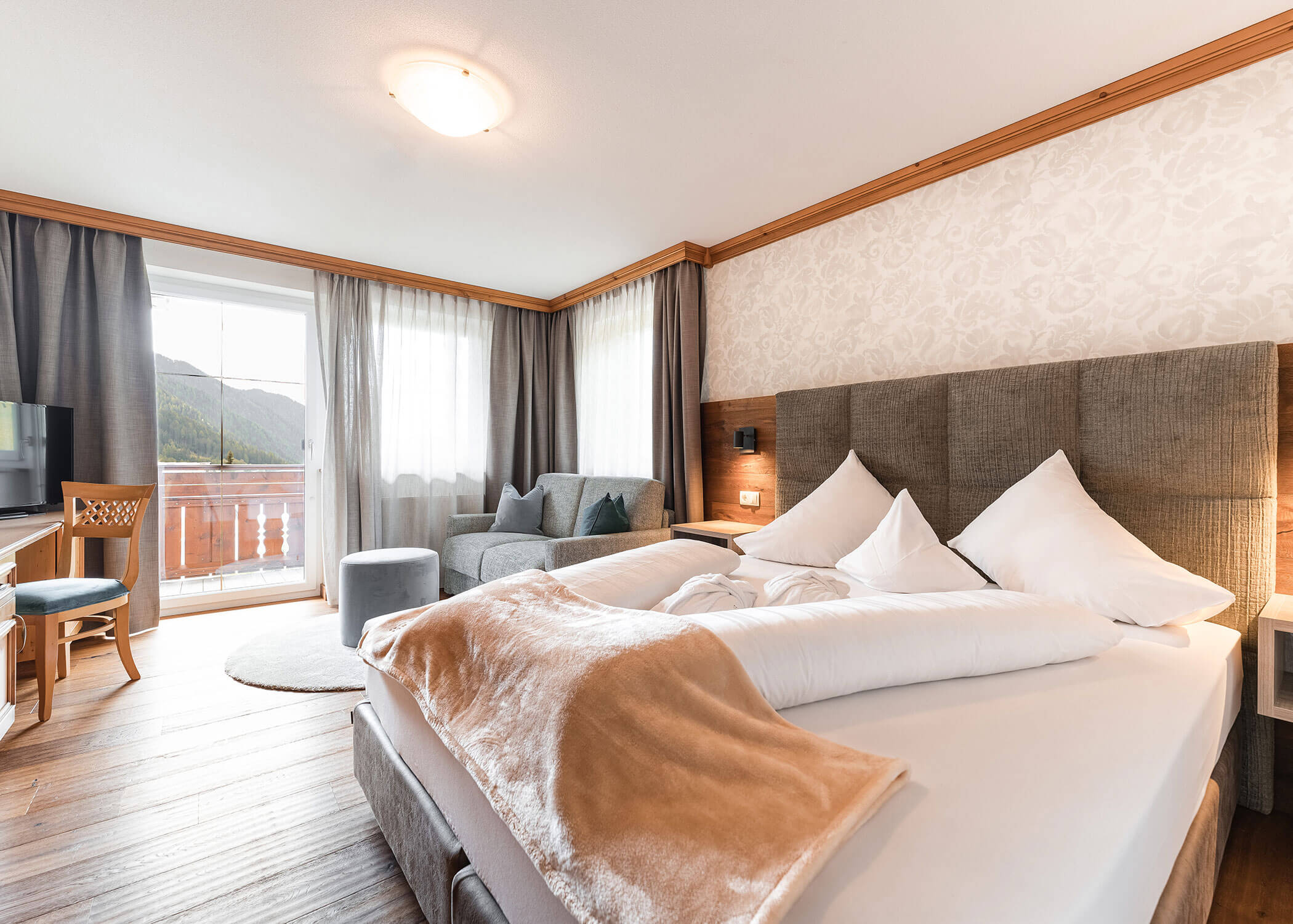 Helles Hotelzimmer mit einem großen Bett, Sofa, Schreibtisch und Balkon mit Bergblick. - Hotel Magdalenahof