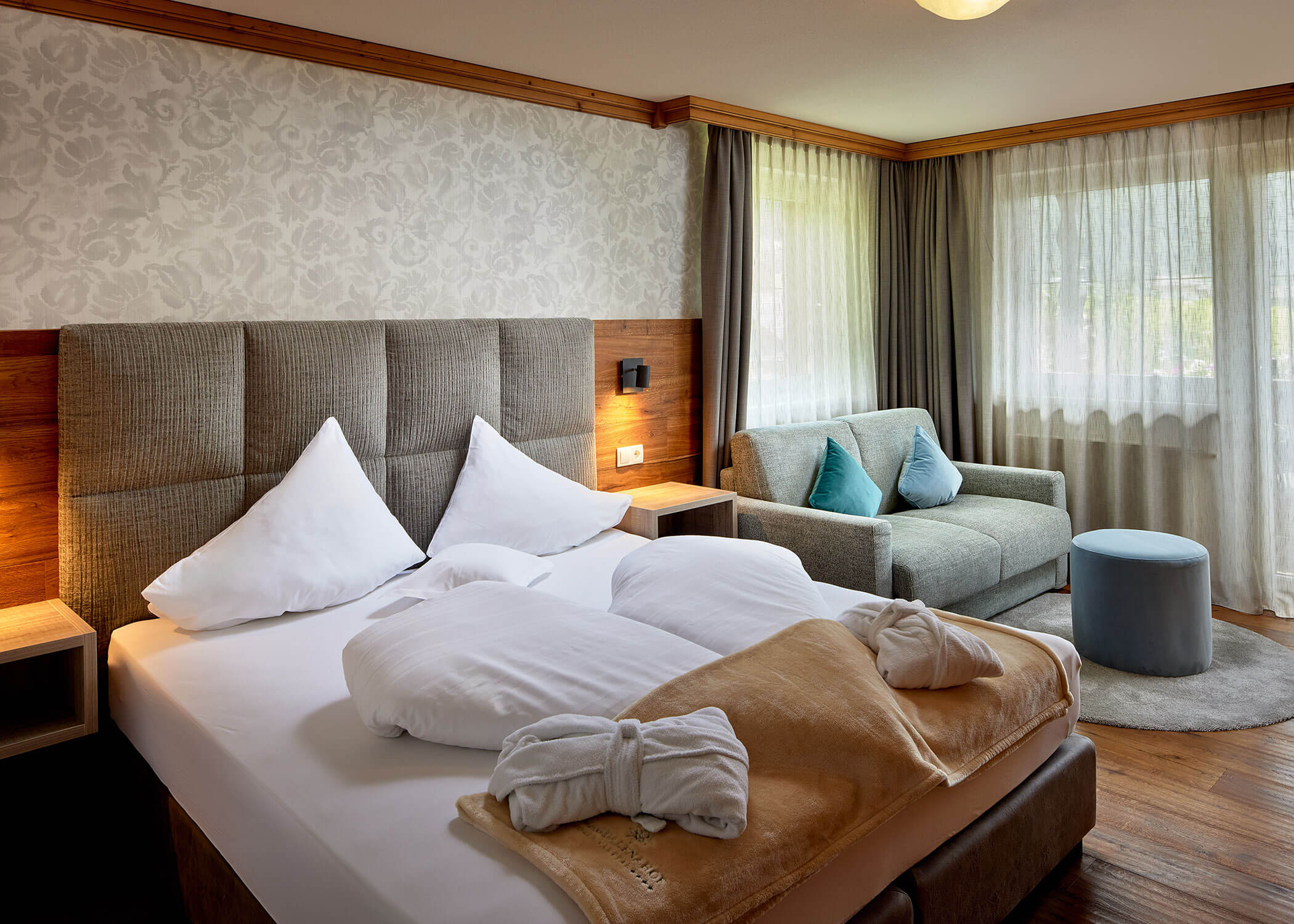 Helles Hotelzimmer mit einem Doppelbett, Bademänteln, einem Sofa, großen Fenstern und eleganter Einrichtung. - Hotel Magdalenahof