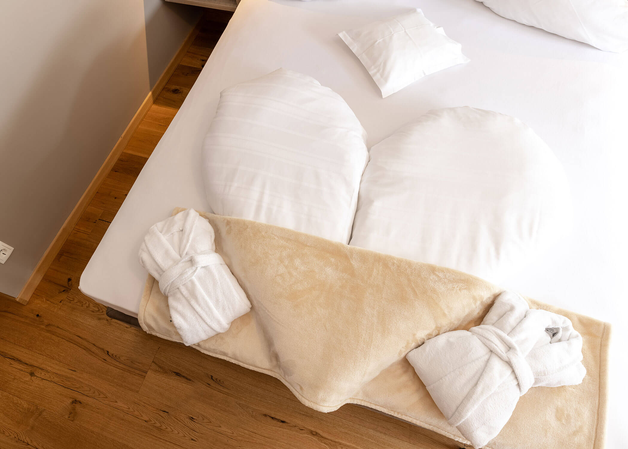 Zwei Handtücher in Form von Schwänen und Kissen, die ein Herz bilden, auf einem sauber gemachten Hotelbett mit einer beigen Decke. - Hotel Magdalenahof