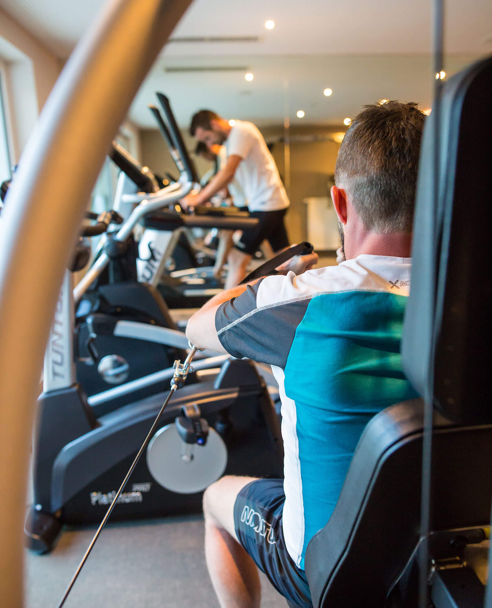 Zwei Männer trainieren in einem Fitnessstudio, der eine an einem Rudergerät, der andere auf einem Laufband. - Hotel Magdalenahof