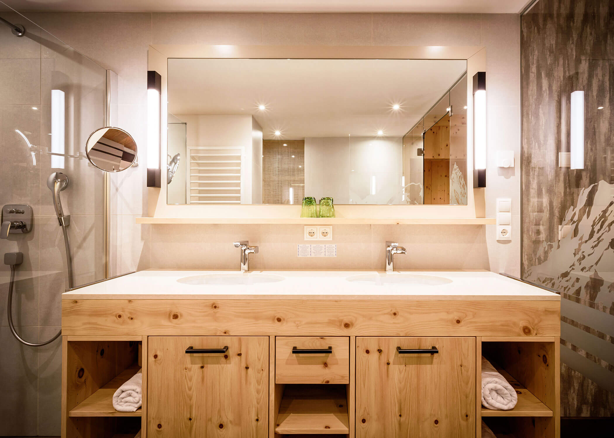 Modernes Bad mit großem Spiegel, Doppelwaschbecken, Holzschränken und Wandleuchten. - Hotel Magdalenahof