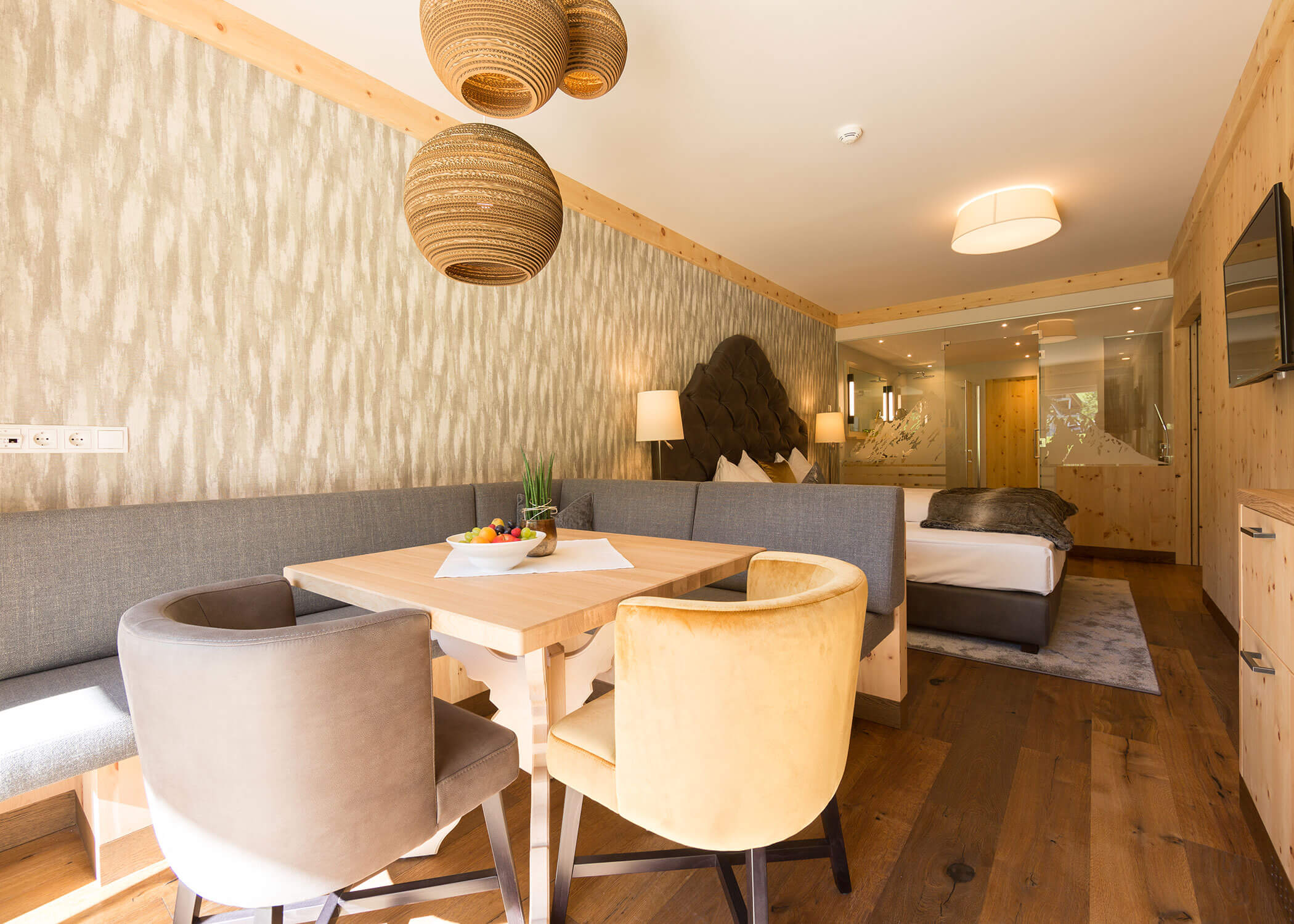 Helles Hotelzimmer mit modernem Holzdekor, Esstisch, Stühlen, Bett und großen Fenstern, die das Sonnenlicht hereinlassen. - Hotel Magdalenahof