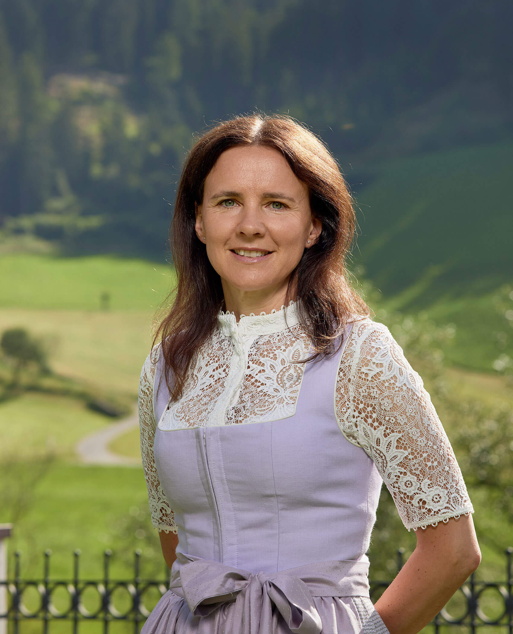 Frau in spitzenbesetztem Kleid im Freien mit grünen Hügeln und Bäumen im Hintergrund. - Hotel Magdalenahof