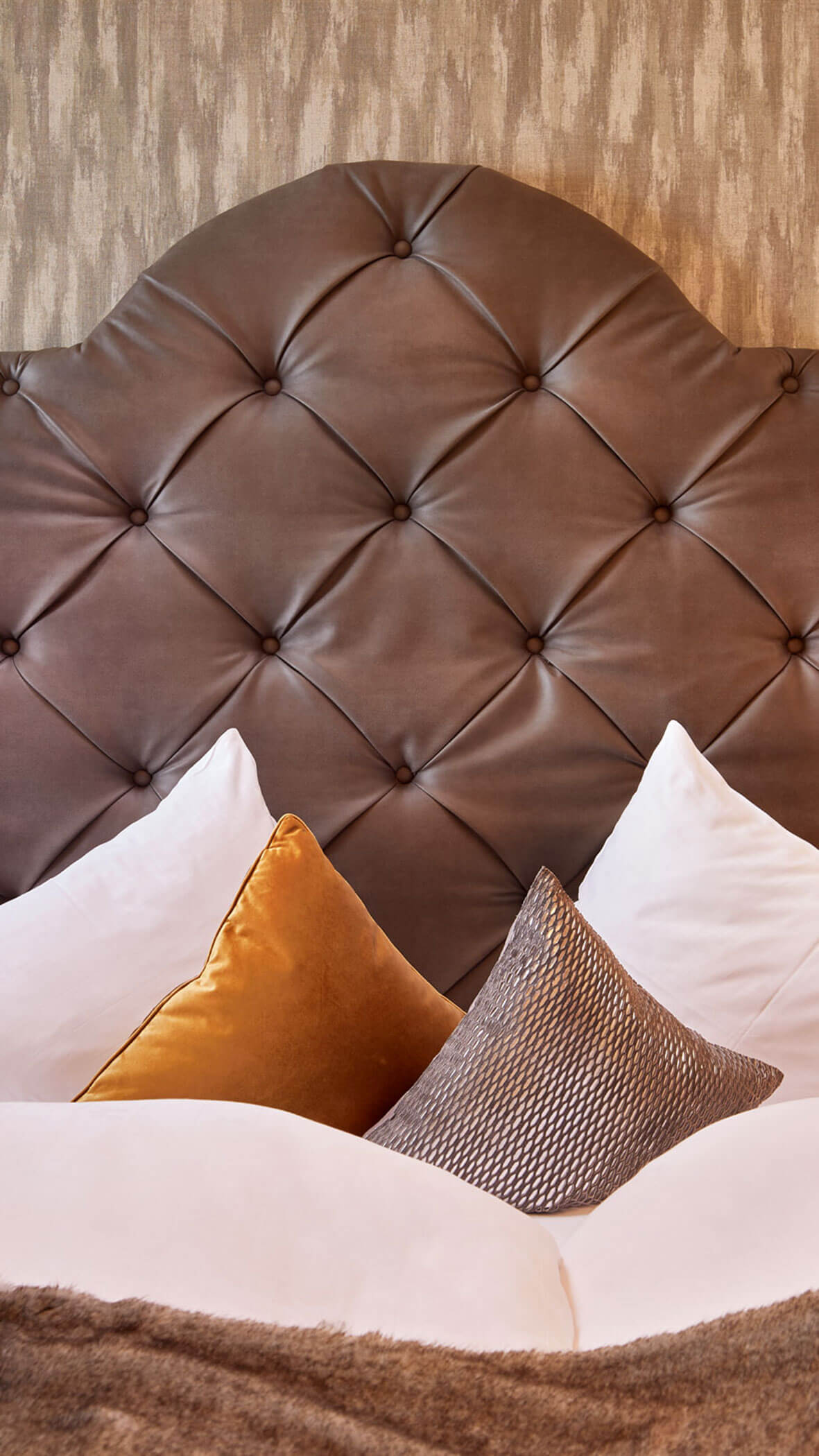 Letto in peluche con cuscini bianchi, un cuscino in velluto dorato, un cuscino grigio e una testata in pelle trapuntata. - Hotel Magdalenahof