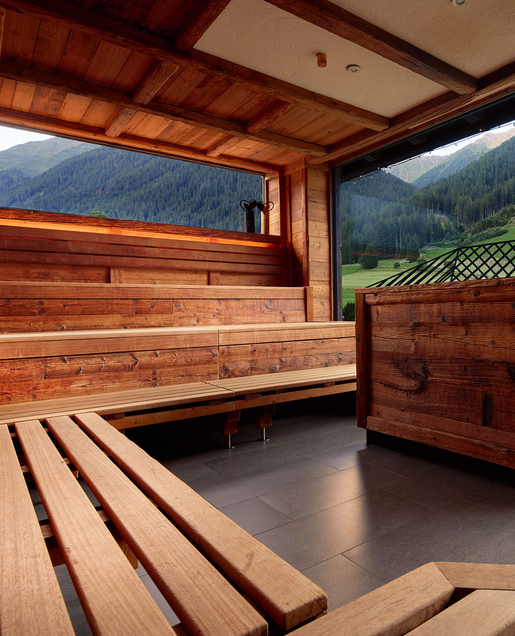 Wooden sauna interior with benches and large open window overlooking green hills and mountains. - Hotel Magdalenahof