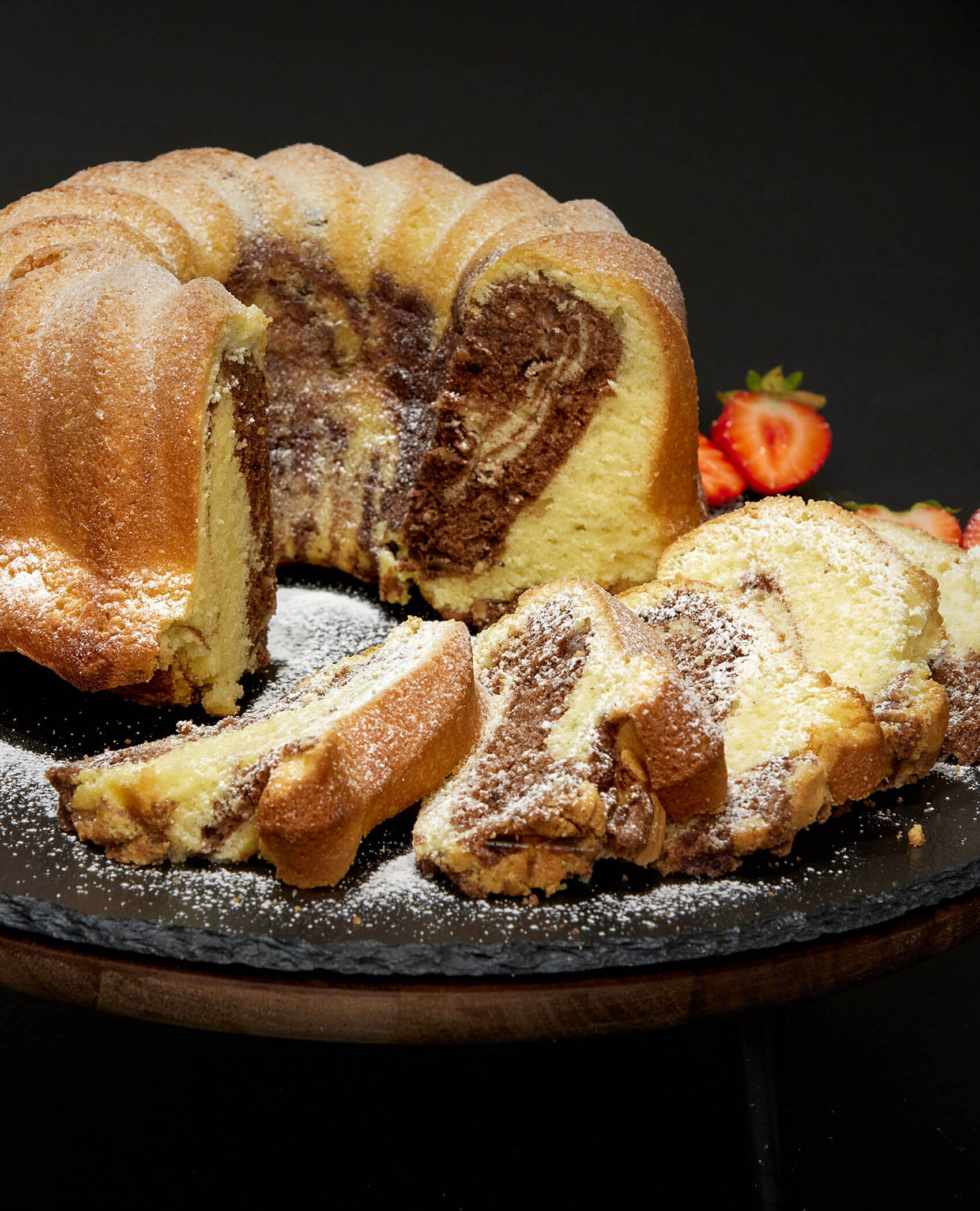 Ein Marmorkuchen, der in Scheiben geschnitten und mit Puderzucker bestäubt wurde, mit Erdbeeren im Hintergrund. - Hotel Magdalenahof