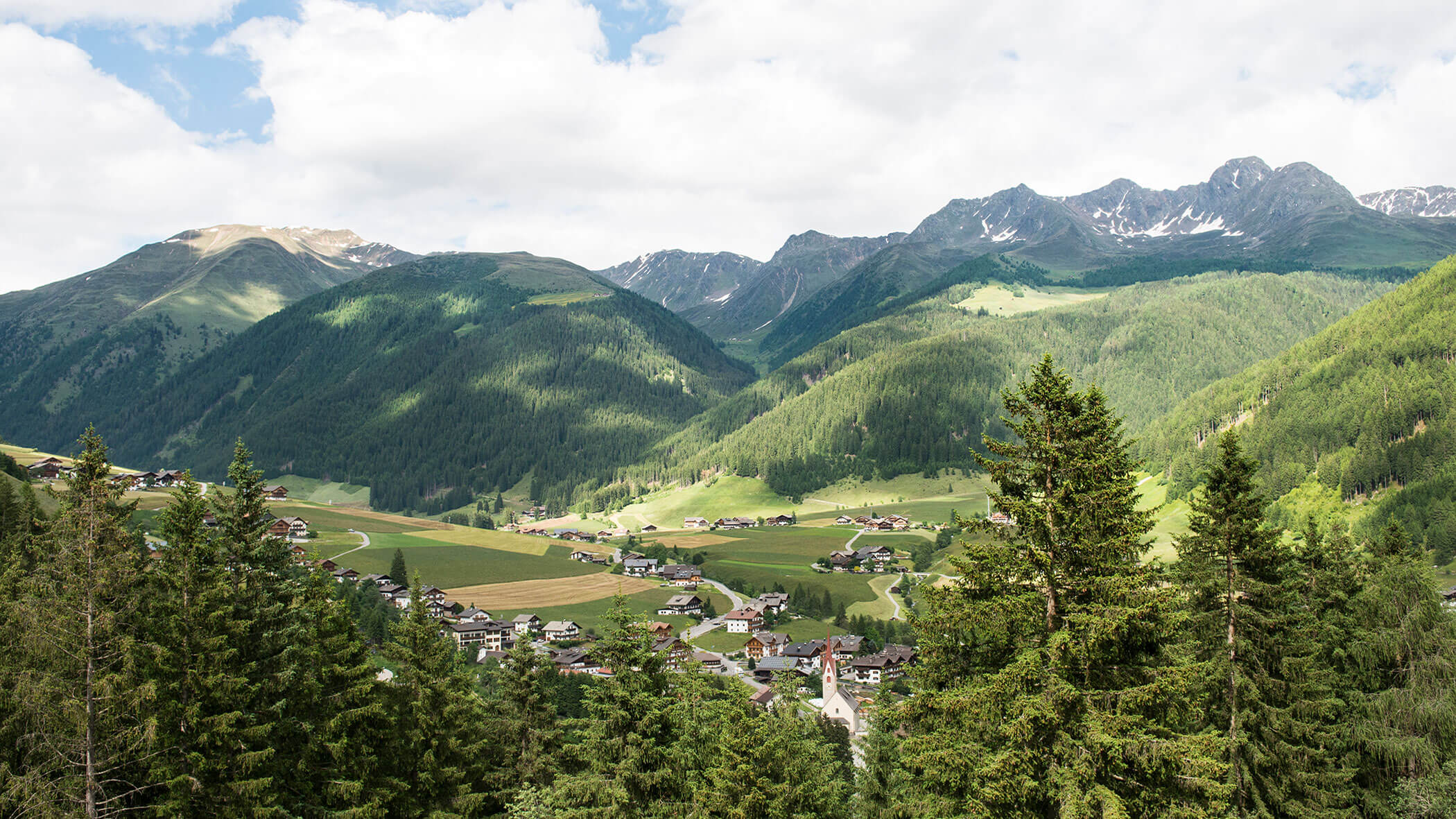 Ein kleines Dorf, eingebettet in ein grünes Tal mit hohen Bergen und Wäldern im Hintergrund. - Hotel Magdalenahof