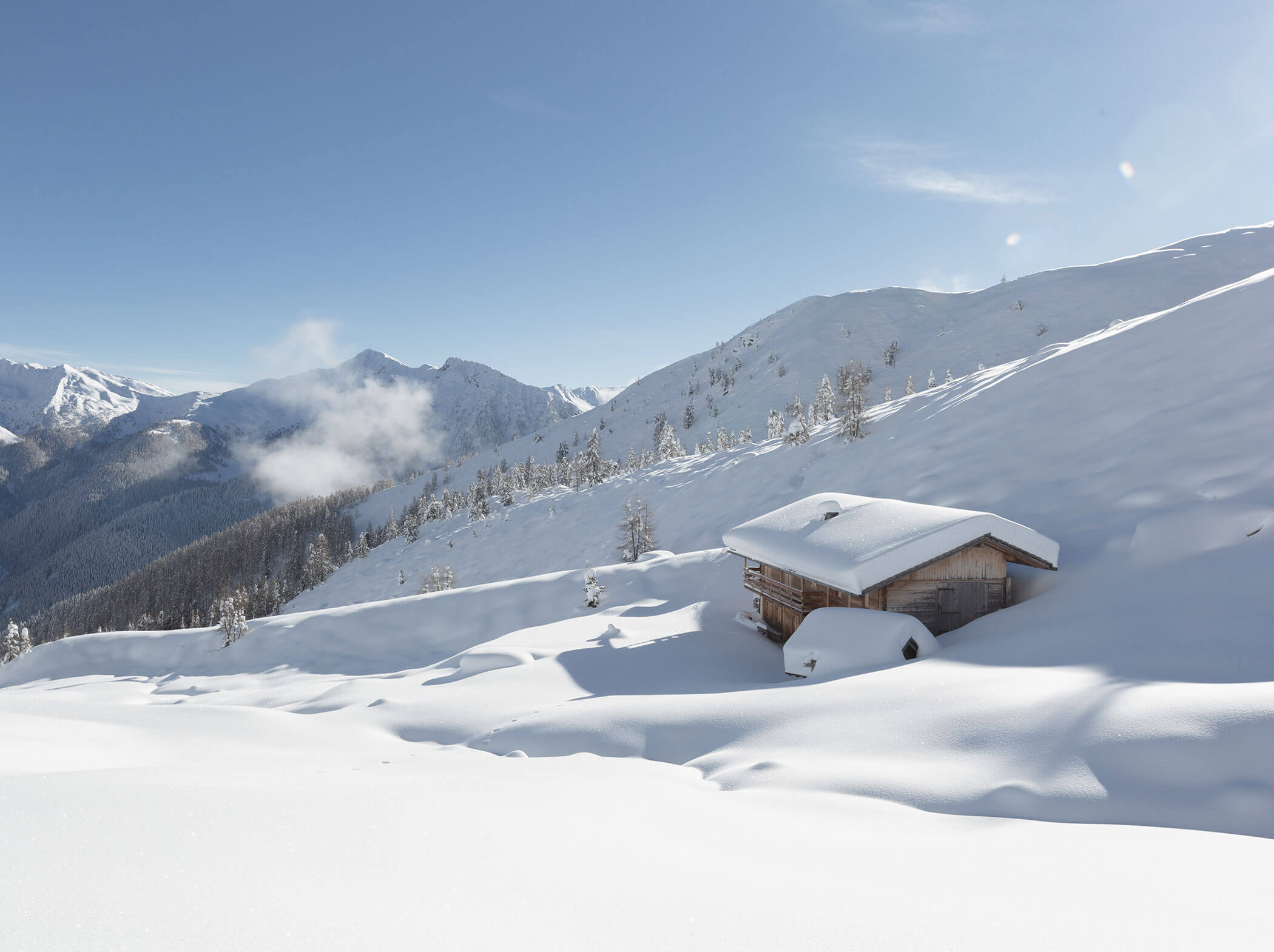 Eine schneebedeckte Holzhütte und ein Auto stehen an einem verschneiten Berghang unter einem strahlend blauen Himmel. - Hotel Magdalenahof