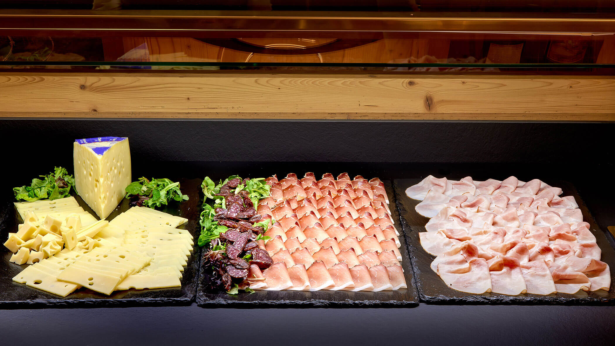 Drei Tabletts mit Käse-, Wurst- und Prosciuttoscheiben, garniert mit Grünzeug auf einem Buffet. - Hotel Magdalenahof