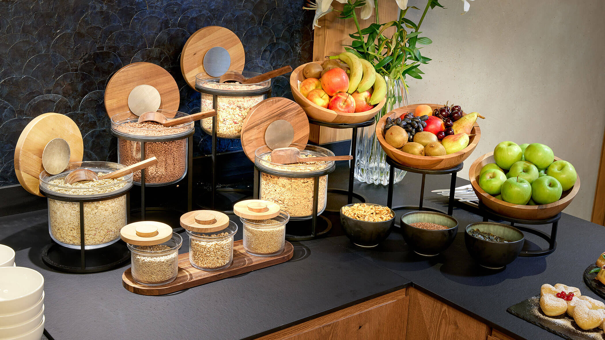 Frühstücksbuffet mit Gläsern mit Müsli, Schalen mit Obst und verschiedenen Nüssen auf einer Arbeitsplatte. - Hotel Magdalenahof
