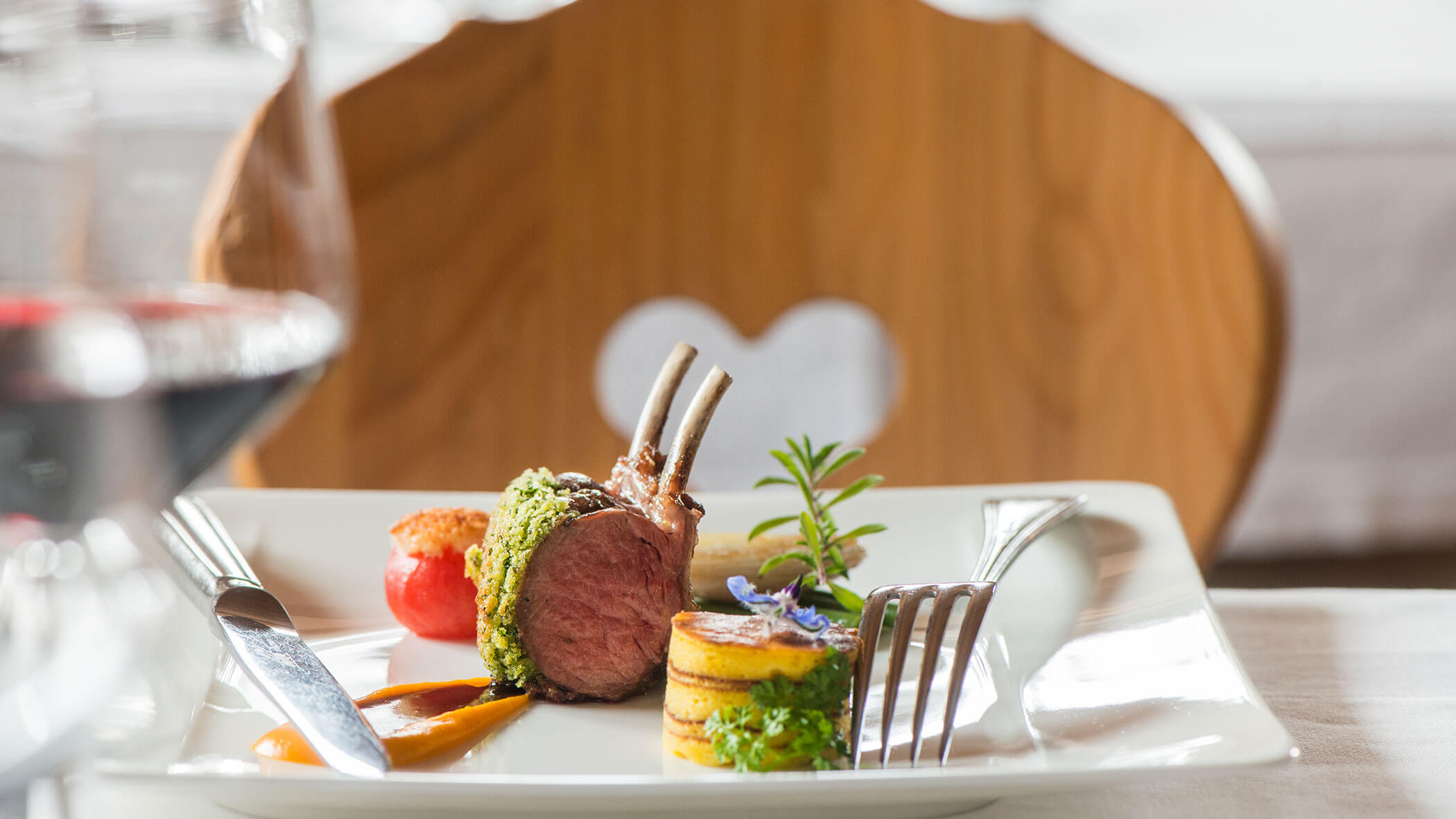 Ein Gourmet-Lammgericht mit Gemüse, garniert mit Kräutern, auf einem weißen quadratischen Teller mit Besteck. - Hotel Magdalenahof