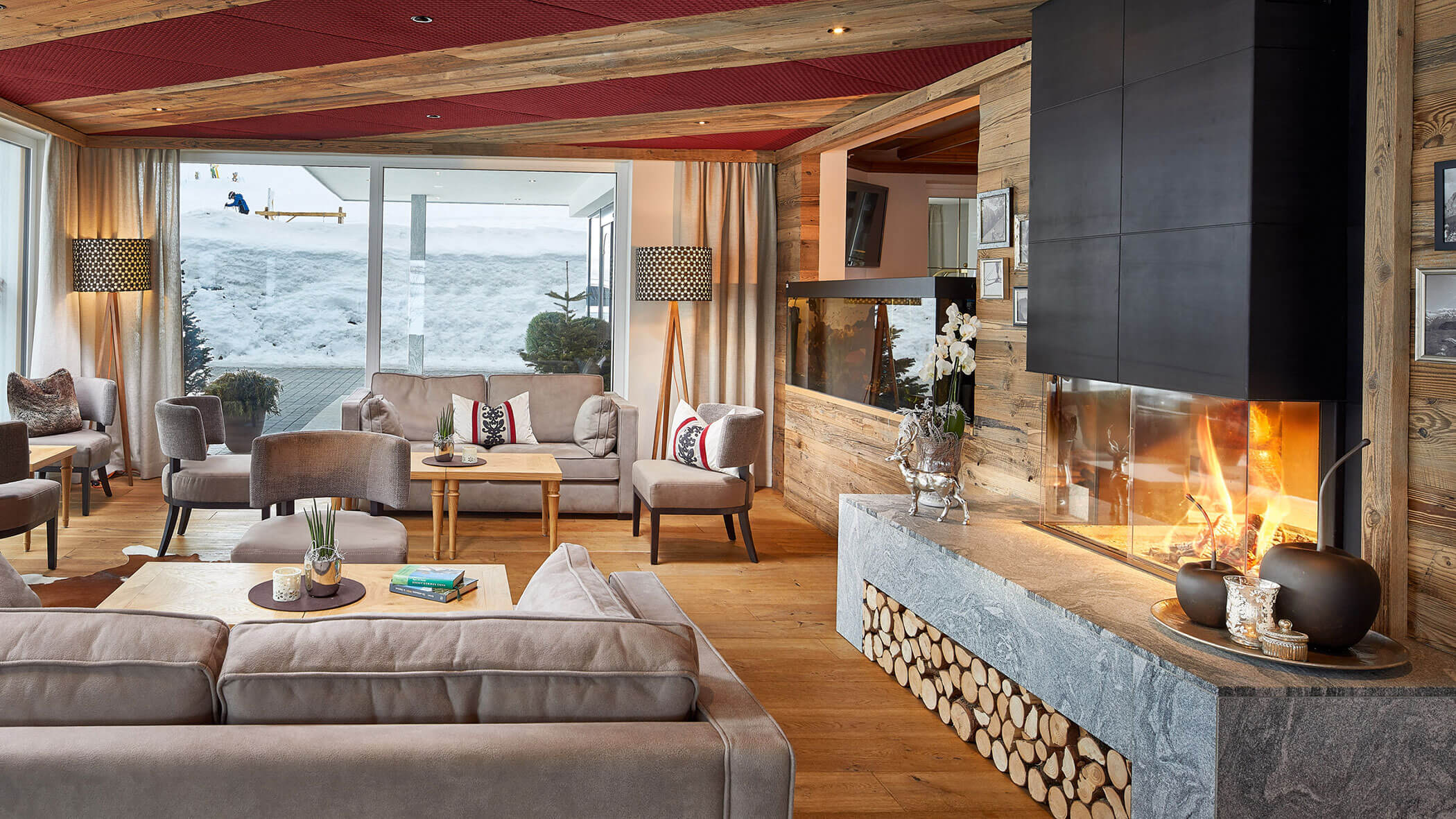Gemütliches Wohnzimmer mit Kamin, Holzwänden, großen Fenstern und sichtbarem Schnee draußen. - Hotel Magdalenahof