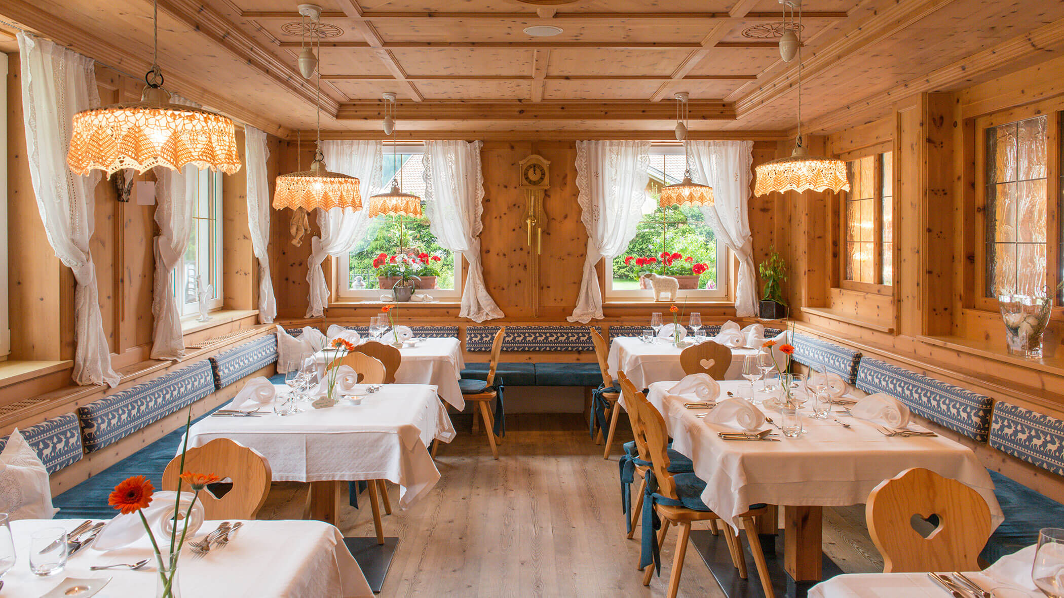 Gemütliches Holzrestaurant mit weißen Tischtüchern, Stühlen mit Rückenlehne und großen Fenstern mit Spitzenvorhängen. - Hotel Magdalenahof
