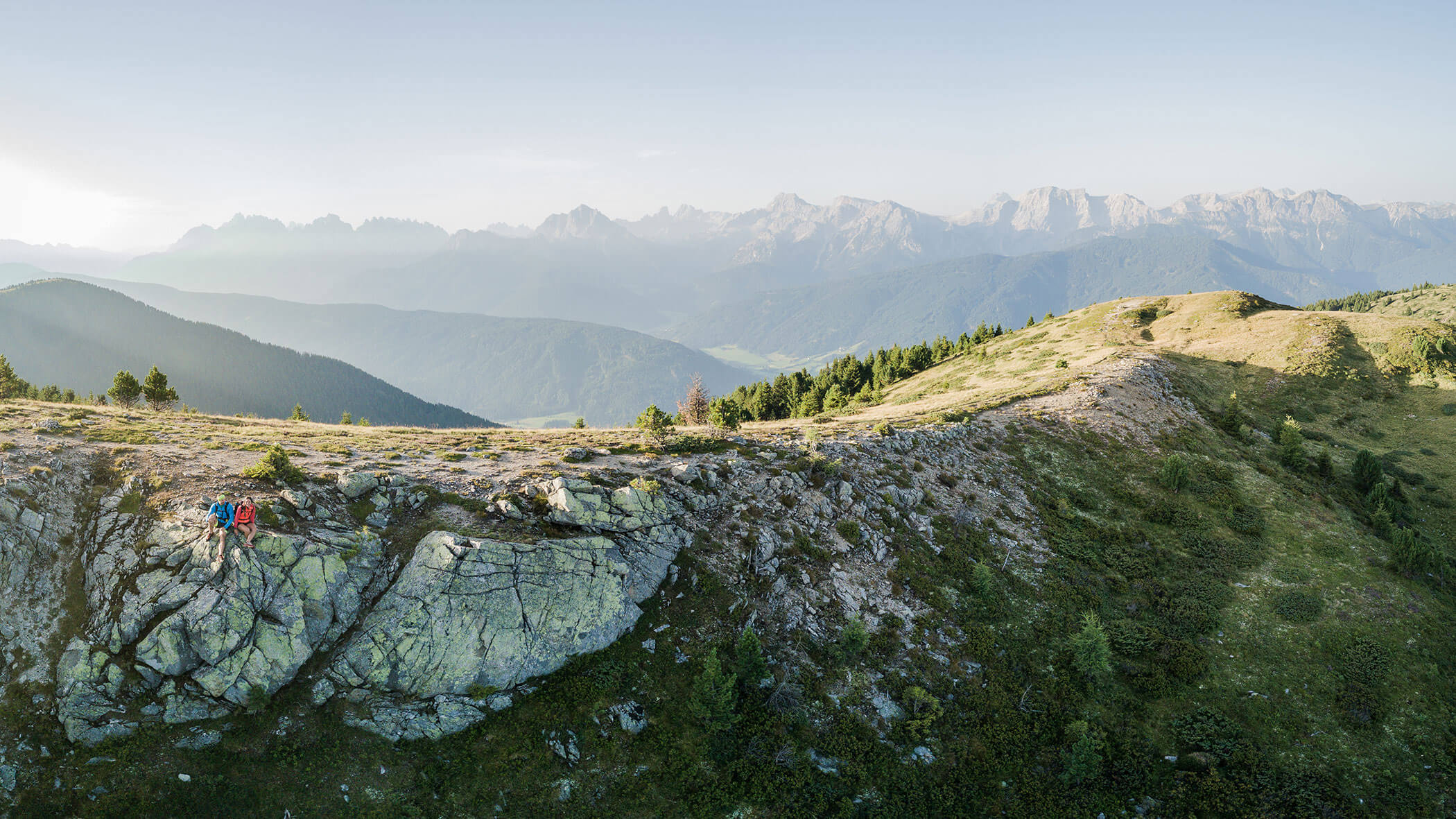 Wanderer wandern entlang eines felsigen, grasbewachsenen Bergrückens mit fernen Bergketten unter einem klaren Himmel. - Hotel Magdalenahof