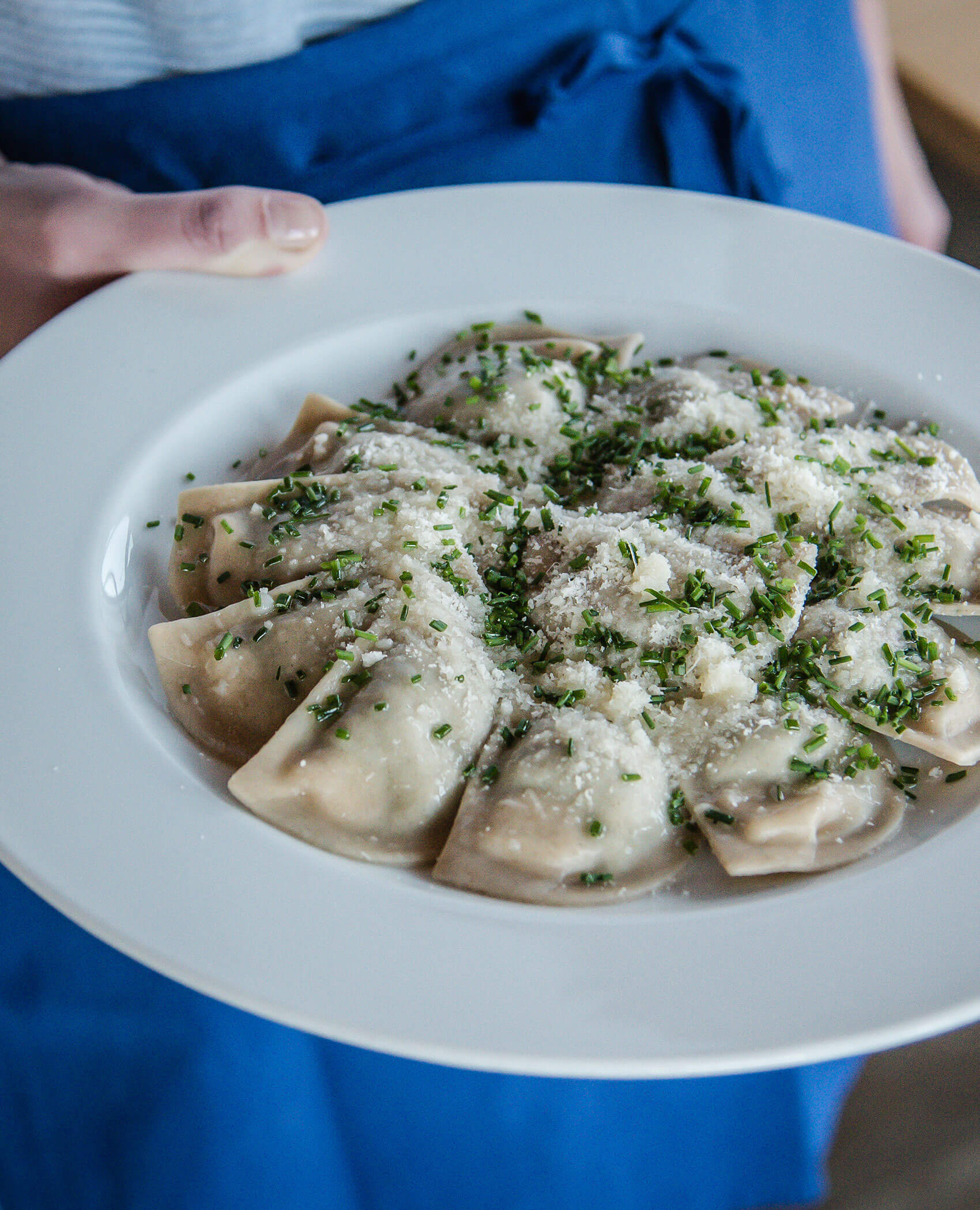 Eine Person hält einen Teller mit Schlutzkrapfen, garniert mit geriebenem Käse und gehackten Kräutern. - Hotel Magdalenahof
