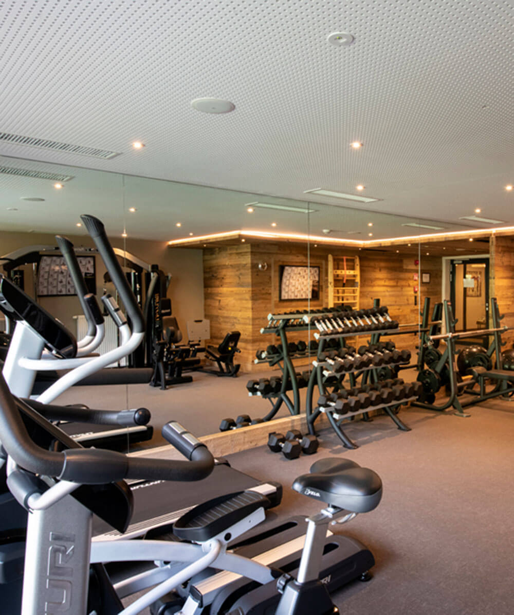 Modernes Fitnessstudio mit Kardiogeräten, freien Gewichten und großen Spiegeln an den Wänden, in denen sich die Geräte spiegeln. - Hotel Magdalenahof