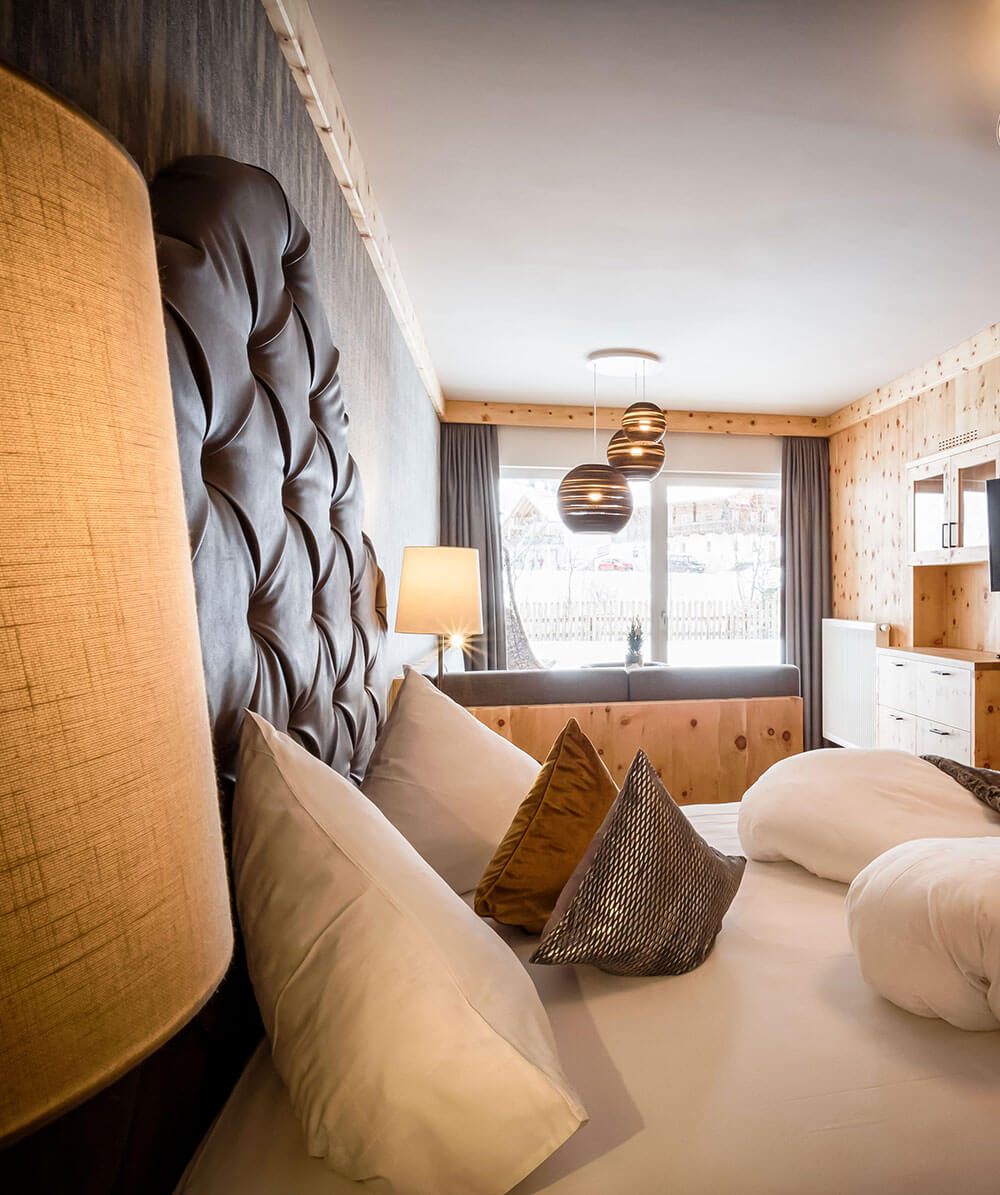 Gemütliches Hotelzimmer mit getuftetem Kopfteil, Kissen, moderner Beleuchtung und großen Fenstern mit Panoramablick. - Hotel Magdalenahof