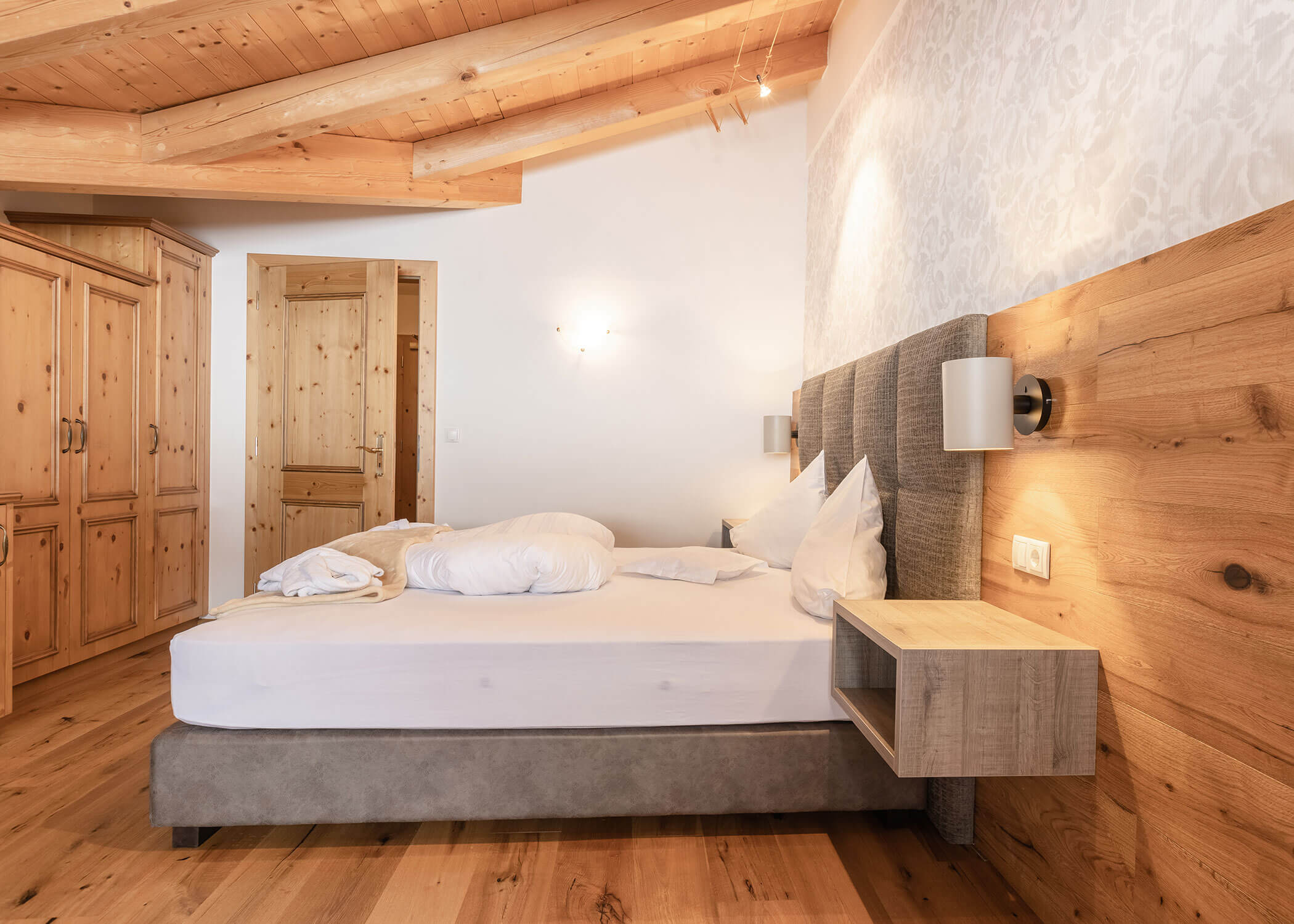 Gemütliches Schlafzimmer mit einem zerwühlten Bett, Holzmöbeln und hellen, holzgetäfelten Wänden und Decken. - Hotel Magdalenahof