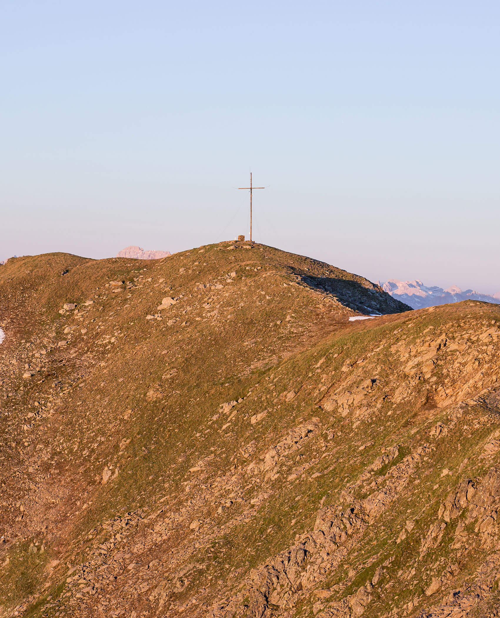 Ein großes Kreuz steht auf einem felsigen Berggipfel unter einem klaren Himmel bei Sonnenuntergang. - Hotel Magdalenahof